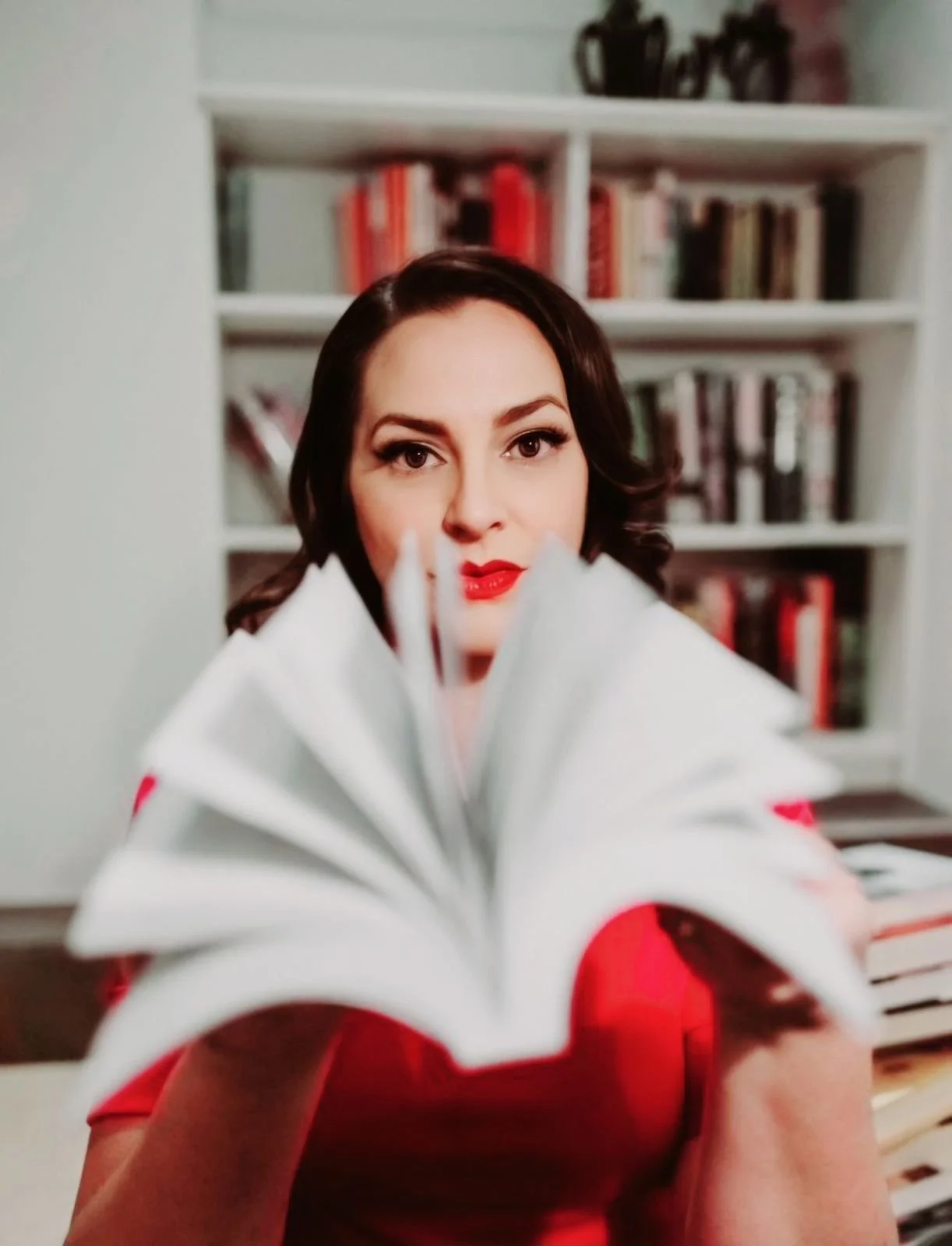 Evelyn Rose, red lips, behind the pages of an open book